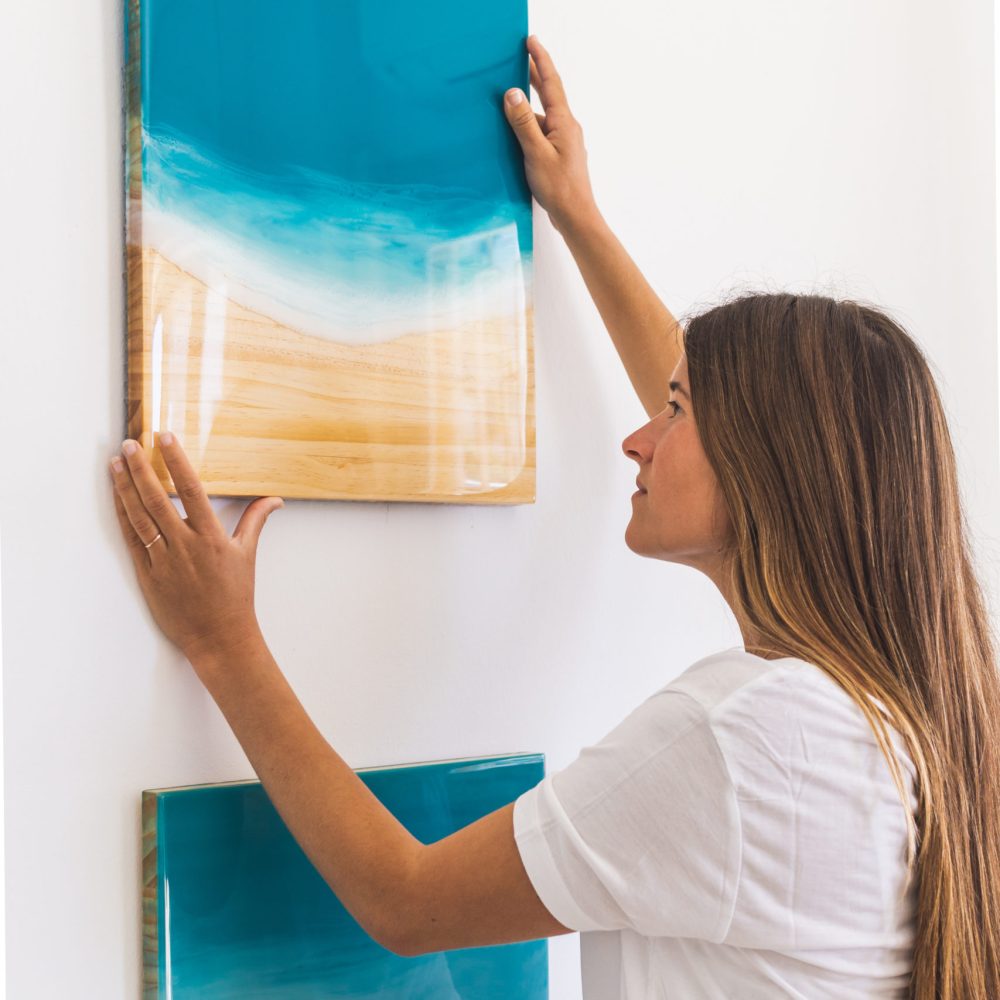 Une artiste accroche une peinture en résine sur un mur blanc